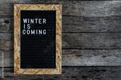 Letter board with white lettering winter is coming on old wooden background.