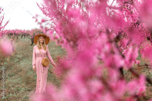 Spring Beautiful romantic girl in fashion dress standing in blooming peach trees.Spring concept.