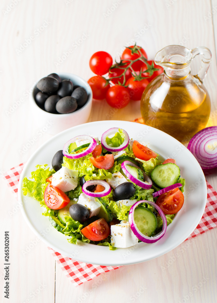 Fresh Greek salad made of cherry tomato, ruccola, arugula, feta, olives, cucumbers, onion and spices. Caesar salad in a white bowl on wooden background. Healthy organic diet food concept.