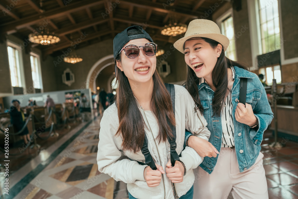 Two beautiful asian girls commute walking in railway train union station talking and laughing. Lifestyle tourism and friendship concepts. young happy women travelers arms in arms historical building