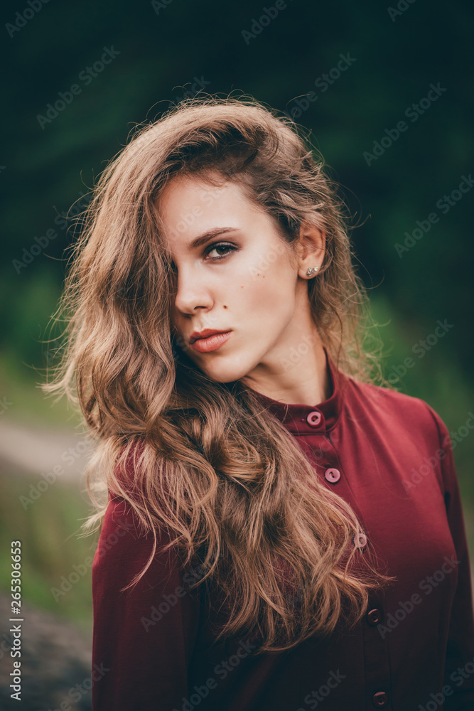 Naklejka premium Beautiful girl with curly natural hair enjoy nature in forest. Dreamer lady in burgundy dress on green background. Inspired girl. Female face portrait. Sun in hair in autumn. Vintage portrait.