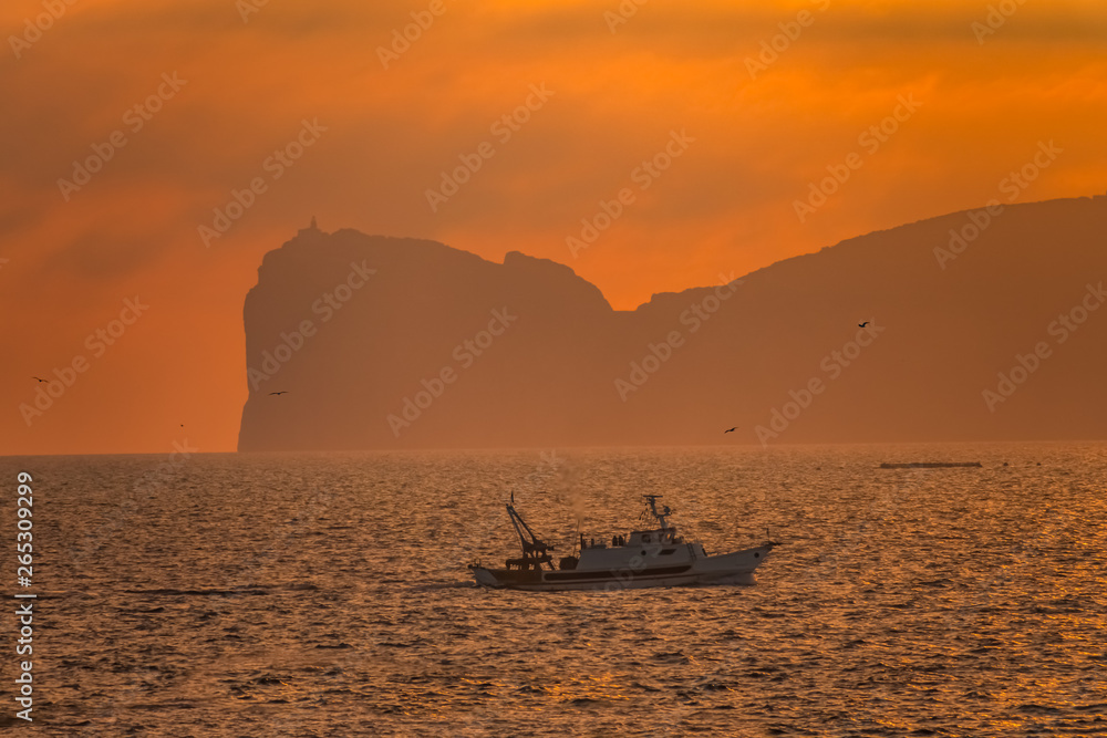 A fishing boats crosses the waters in front of Capo Caccia near Alghero, Sardinia, Italy