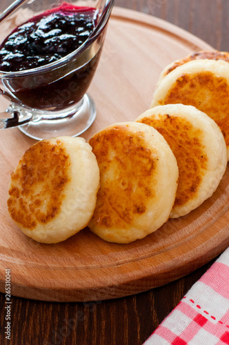 Cheese pancakes with currant jam, on a wooden plate, vertical photo