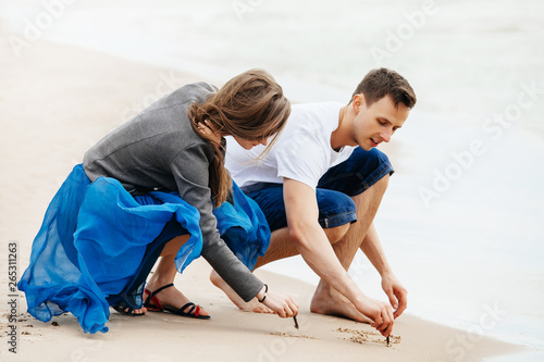 Young couple on the beach drawing in sand.