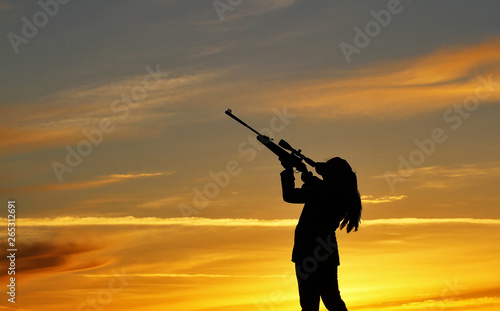 Silhouette of a girl with a rifle on the background of a beautiful sunset, the girl shoots a gun