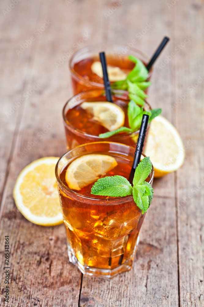 Traditional iced tea with lemon, mint leaves and ice cubes in three glasses on rustic wooden table. Traditional iced tea with lemon, mint leaves and ice cubes in three glasses on rustic wooden table.