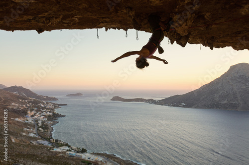 Female rock climber hanging upside down on challenging route in cave at sunset