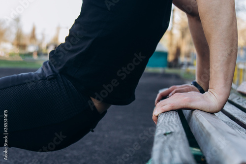 A young man in black clothes is exercising outdoors close up. fitness athlete on the sports field. training with projectiles. warm up body preparation for the summer