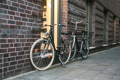 Bicycles are parked next to a brick wall of a building on a city street.
