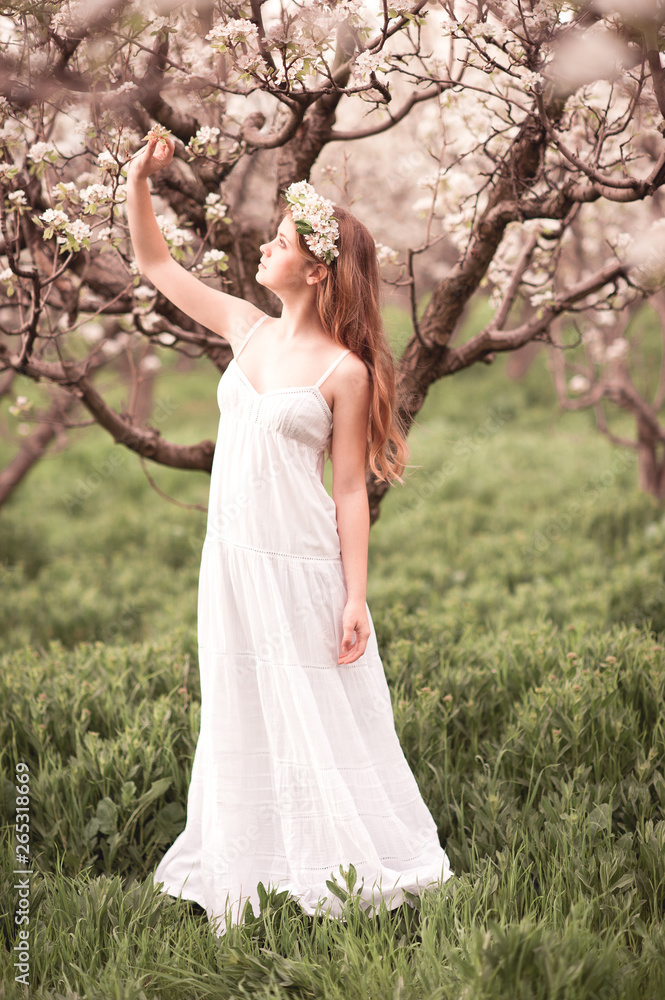 Young girl wearing white dress and loral wreath standing at pear orchard. Spring season. Young girl wearing white dress and loral wreath standing at pear orchard. Spring season.