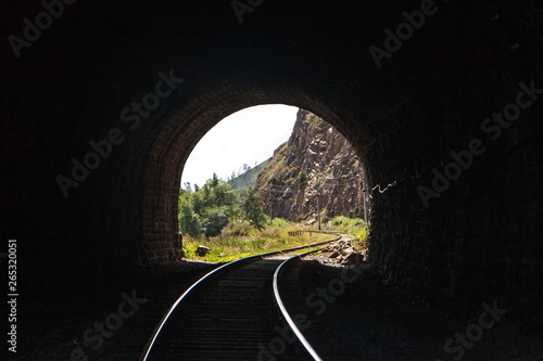 light with a landscape at the end of a stone railway tunnel with beautifully lit rails in the mountains