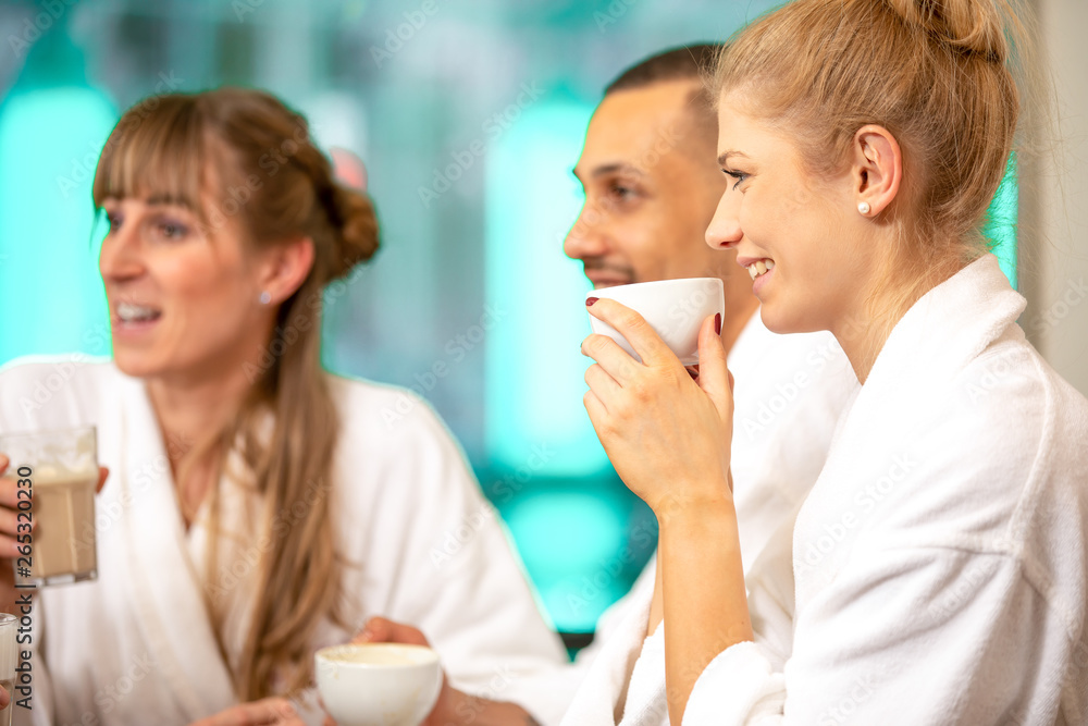 Young handsome group are doing wellness in a bathing landscape. They drink coffee, cappuccino and champagne with a bathrobe in the sauna