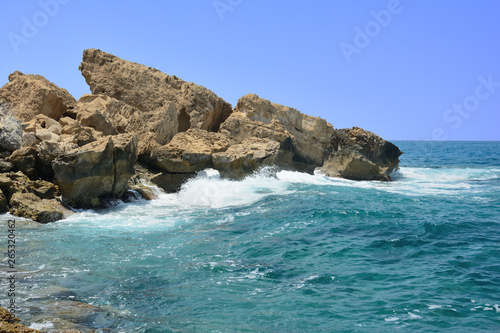 the waves running on the stony coast against the background of the blue sky