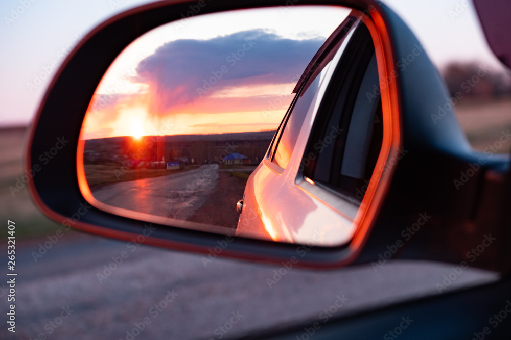 The reflection of the setting sun in the rearview mirror of the car