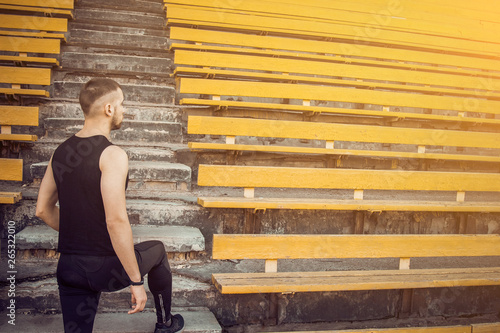 A slender young man in black sportswear stands in front of the stairs stadium stands. ready for action, step to victory, challenge © Yuliia