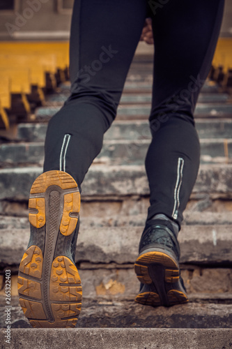 man trains in running on the stairs. Track and field runner in sport uniform training outdoor. athlete, below view. step exercises. vertical. pumped up shanks close up © Yuliia