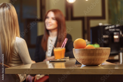 Two beautiful young women drink orange juice and talk while sitting in a cafe bar. The concept of a vegetarian cafe and a healthy lifestyle