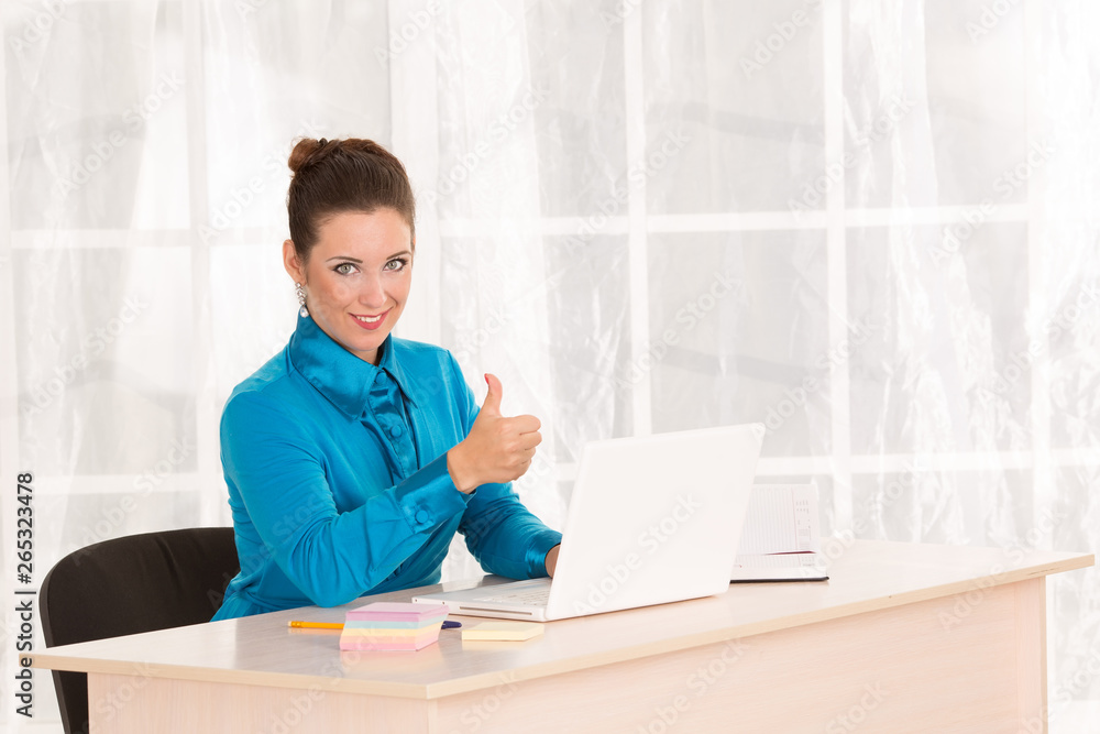 Female office worker. Secretary or manager next to the laptop. Employee works at a desk in an office building. Laptop and notebook for notes on the table. Good mood, everything turned out. Okay. Ok. Female office worker. Secretary or manager next to the laptop. Employee works at a desk in an office building. Laptop and notebook for notes on the table. Good mood, everything turned out. Okay. Ok.