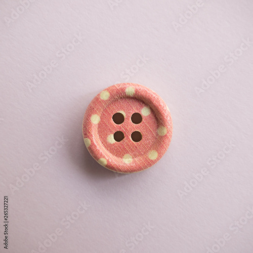 Isolated wooden button with colored colorful dots on a light pink background