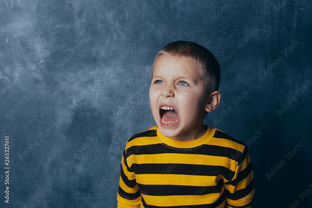 Portrait of a screaming child with open mouth, A little boy poses in front of a gray-blue concrete wall. Portrait of a screaming child with open mouth, A little boy poses in front of a gray-blue concrete wall.