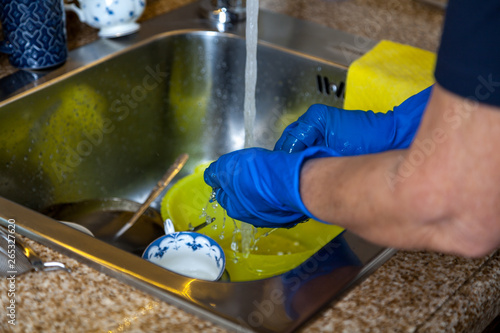 Hands in blue rubber gloves wash dishes in sink