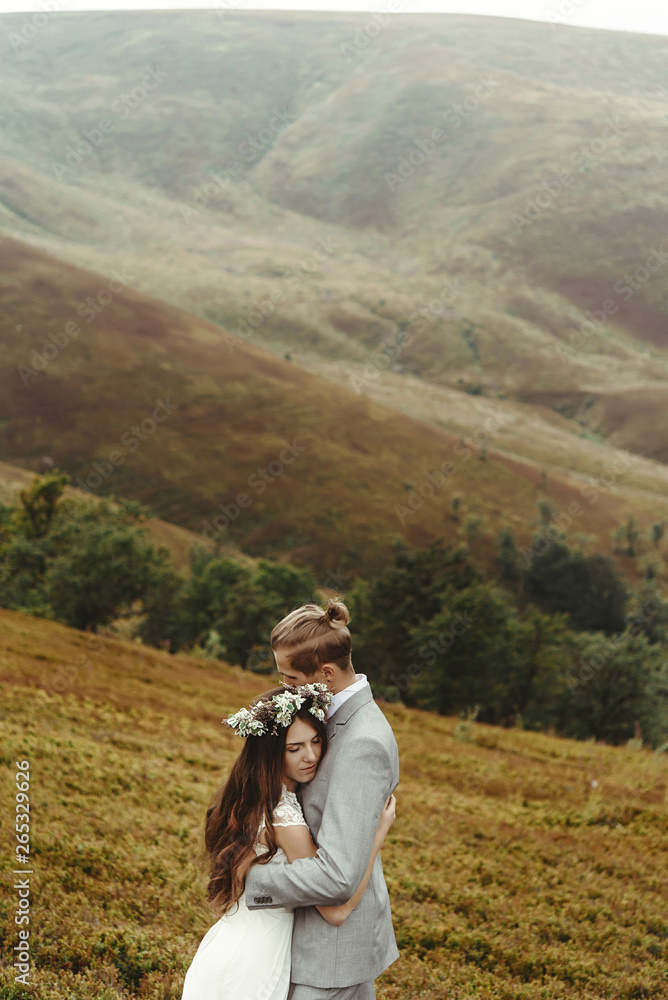 gorgeous bride and stylish groom hugging at sunny landscape,  boho wedding couple, luxury ceremony at mountains with amazing view