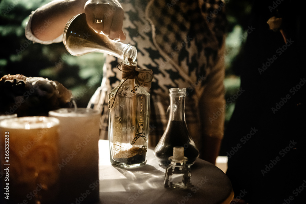 bride and groom holding and pouring  glass jars with sand for wedding tradition ritual at evening reception