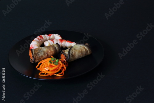 Delicious fried eggplant rolls stuffed with carrots, shrimp necks and pickled carrots on black ceramic plate on black background. Concept — Asia, gourmet, restaurant, table serving.
