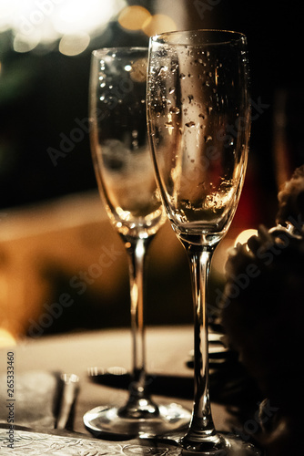 stylish champagne glasses empty on background of warm romantic candle light at evening wedding ceremony