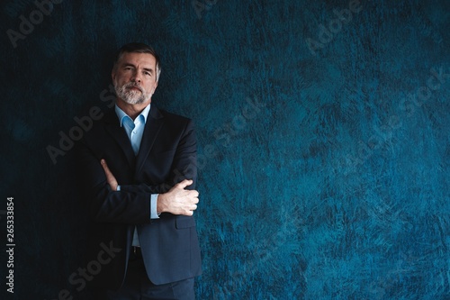 Serious mature man posing in front of a dark blue background with copy space.