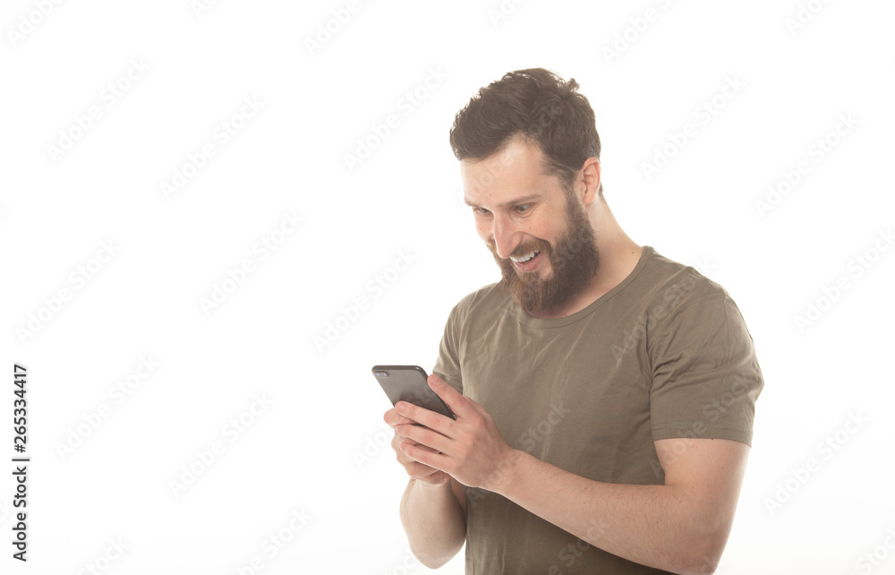 Typing text message. Smiling man with beard standing on white background and holding mobile phone. Typing text message. Smiling man with beard standing on white background and holding mobile phone.