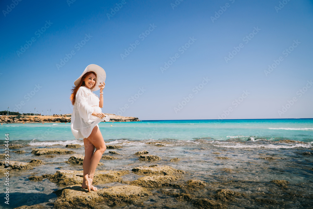 Woman tourist white dress standing on beach with crystal clear water.