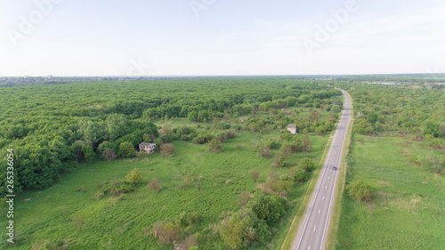 Aerial view of white car driving on country road in forest. The aerial view flew over an old patched two-lane forest road with moving green trees of dense forests growing on both sides. Driving a car