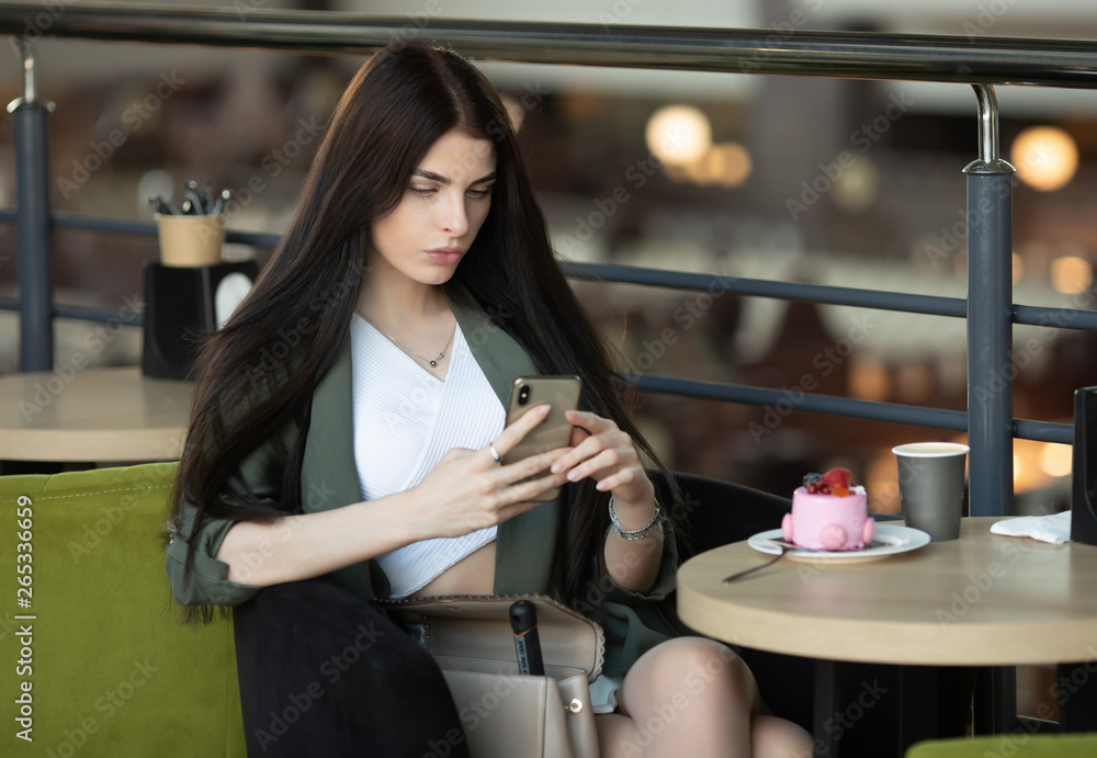 Young businesswoman with cell telephone in hand thinking about something serious while sitting in modern cafe interior. Young businesswoman with cell telephone in hand thinking about something serious while sitting in modern cafe interior.