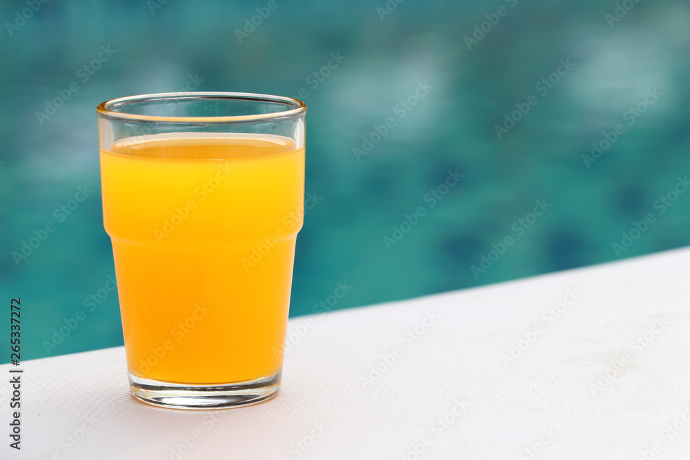 The glass of orange juice is placed on the seat of the chair located by the pool. The glass of orange juice is placed on the seat of the chair located by the pool.