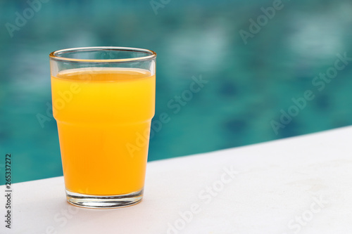 The glass of orange juice is placed on the seat of the chair located by the pool.