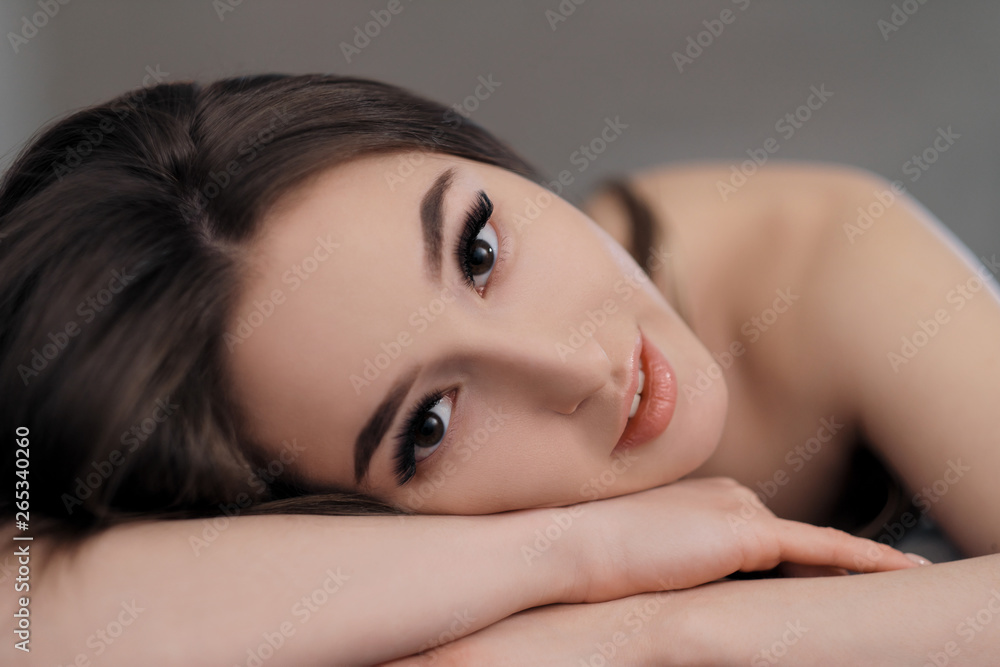 Beautiful brunette girl with brown eyes with bare shoulders lying on the bed. Face close up. Asian and Oriental type of appearance. Beautiful brunette girl with brown eyes with bare shoulders lying on the bed. Face close up. Asian and Oriental type of appearance.