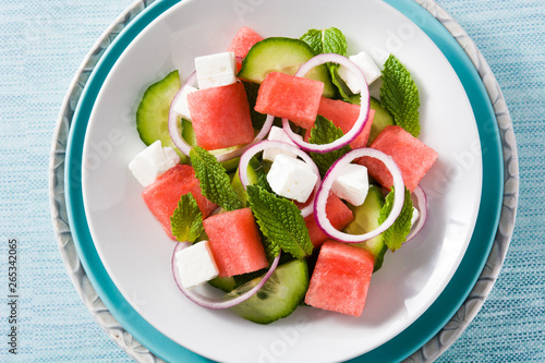 watermelon salad with feta cheese,mint,onion and cucumber on blue background. Top view. Close up