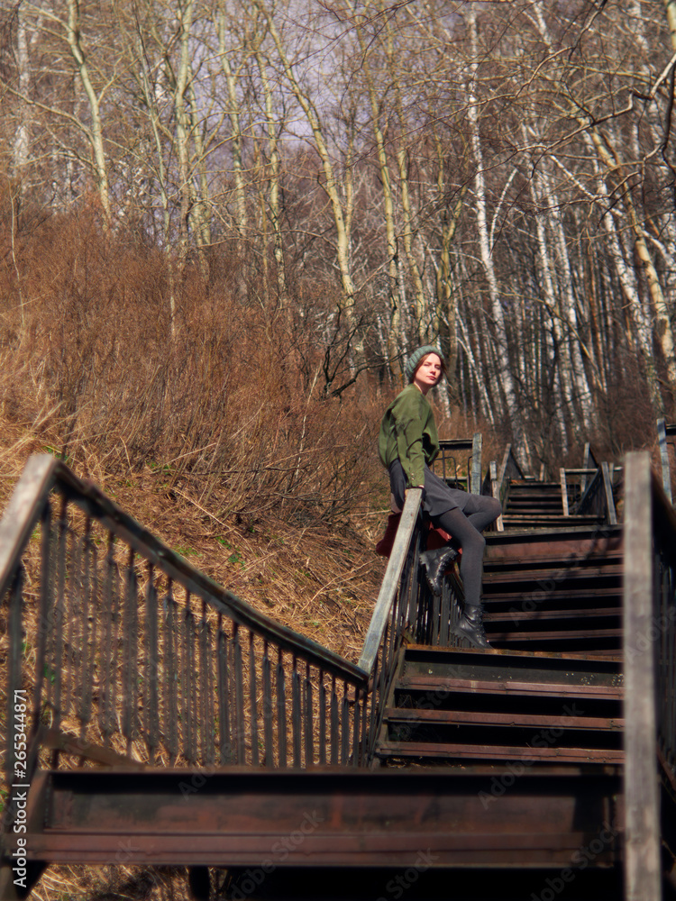 A woman in gray skirt and pantyhose, wearing a green hat, is sitting on the railing of a long staircase. A woman in gray skirt and pantyhose, wearing a green hat, is sitting on the railing of a long staircase.