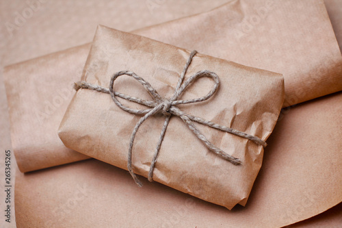 Brown craft package with bow from hemp tie. Wrapped parcel on paper background.