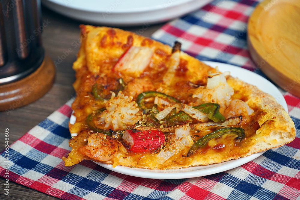 Piece of pizza on white dish plate lay on the table in the restaurant. Piece of pizza on white dish plate lay on the table in the restaurant.