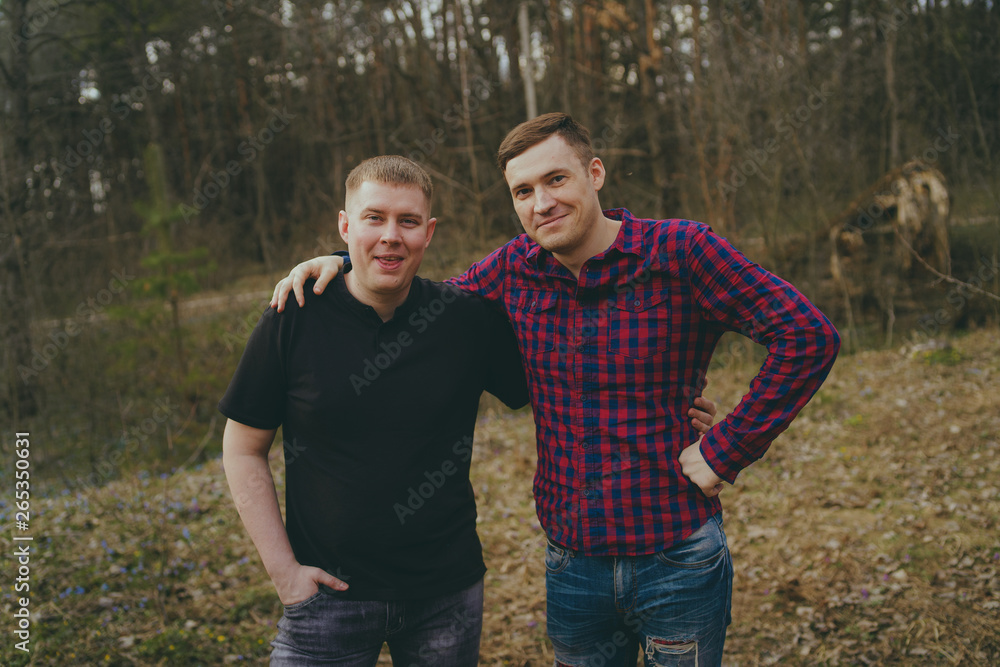 Young smiling friends in modern clothes. Two men posing in the woods. The concept of male friendship Young smiling friends in modern clothes. Two men posing in the woods. The concept of male friendship
