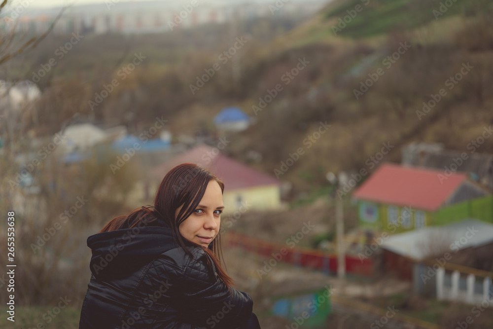 Young woman sitting on green hill Side view of young dreamy female sitting on altitude and looking at suburb in spring day