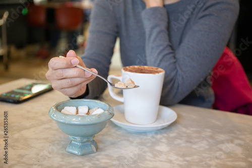 Woman adding sugar cubes in coffee on the table.