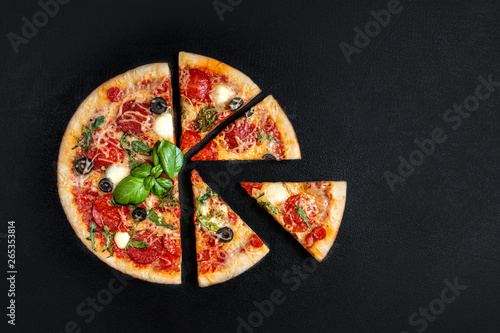 Flatbread pizza with slices on black background. Pepperoni Pizza. Copy space. Top view