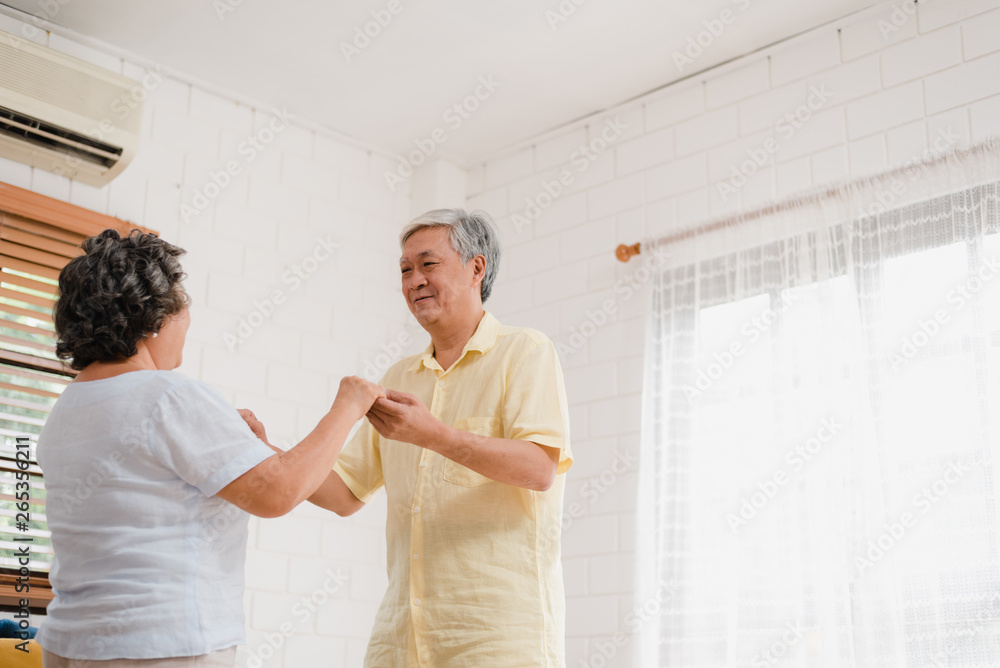 Obraz premium Asian elderly couple dancing together while listen to music in living room at home, sweet couple enjoy love moment while having fun when relaxed at home. Lifestyle senior family relax at home concept.