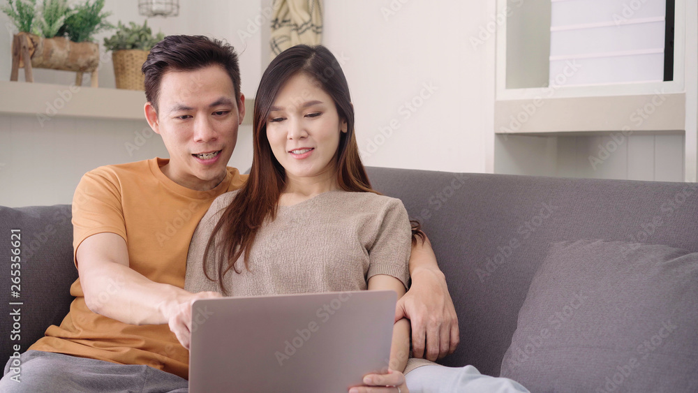 Asian couple using laptop for search web in living room at home, sweet couple enjoy love moment while lying on the sofa when relax at home. Lifestyle couple relax at home concept. Asian couple using laptop for search web in living room at home, sweet couple enjoy love moment while lying on the sofa when relax at home. Lifestyle couple relax at home concept.