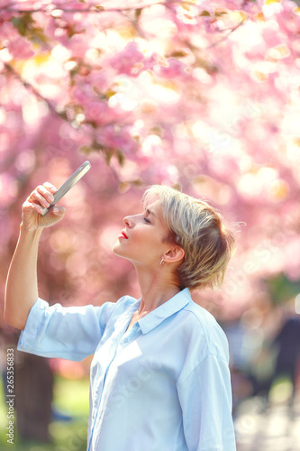 Young attractive blonde girl posing near a blossoming cherry tree. Spring mood.