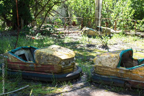 Old broken rusty metal radioactive yellow cars, children's electric cars, abandoned among vegetation, the park of culture and recreation in the city of Pripyat, the Chernobyl disaster, Ukraine. © Serhii Barylo