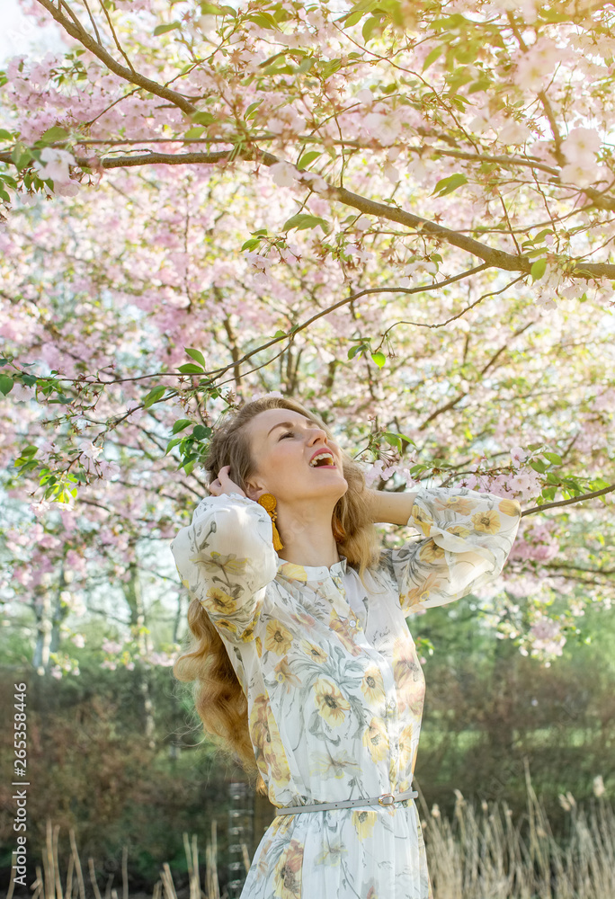 Lovely Beautiful Caucasian Woman in Dress Standing Posing on the Background of Blooming Japan Cherry Blossoms Pastel Pink Sakura Garden Park Fashion Look Springtime Sunny Day Walking Lovely Beautiful Caucasian Woman in Dress Standing Posing on the Background of Blooming Japan Cherry Blossoms Pastel Pink Sakura Garden Park Fashion Look Springtime Sunny Day Walking